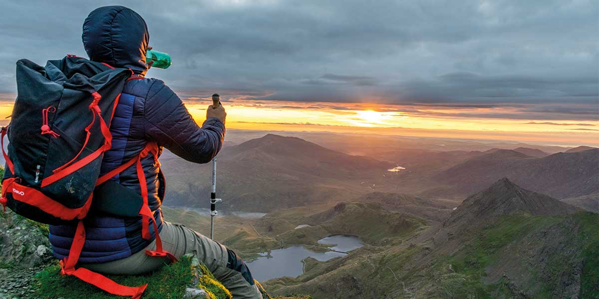 A hiker sitting down at the top of a mountain as the sun comes up