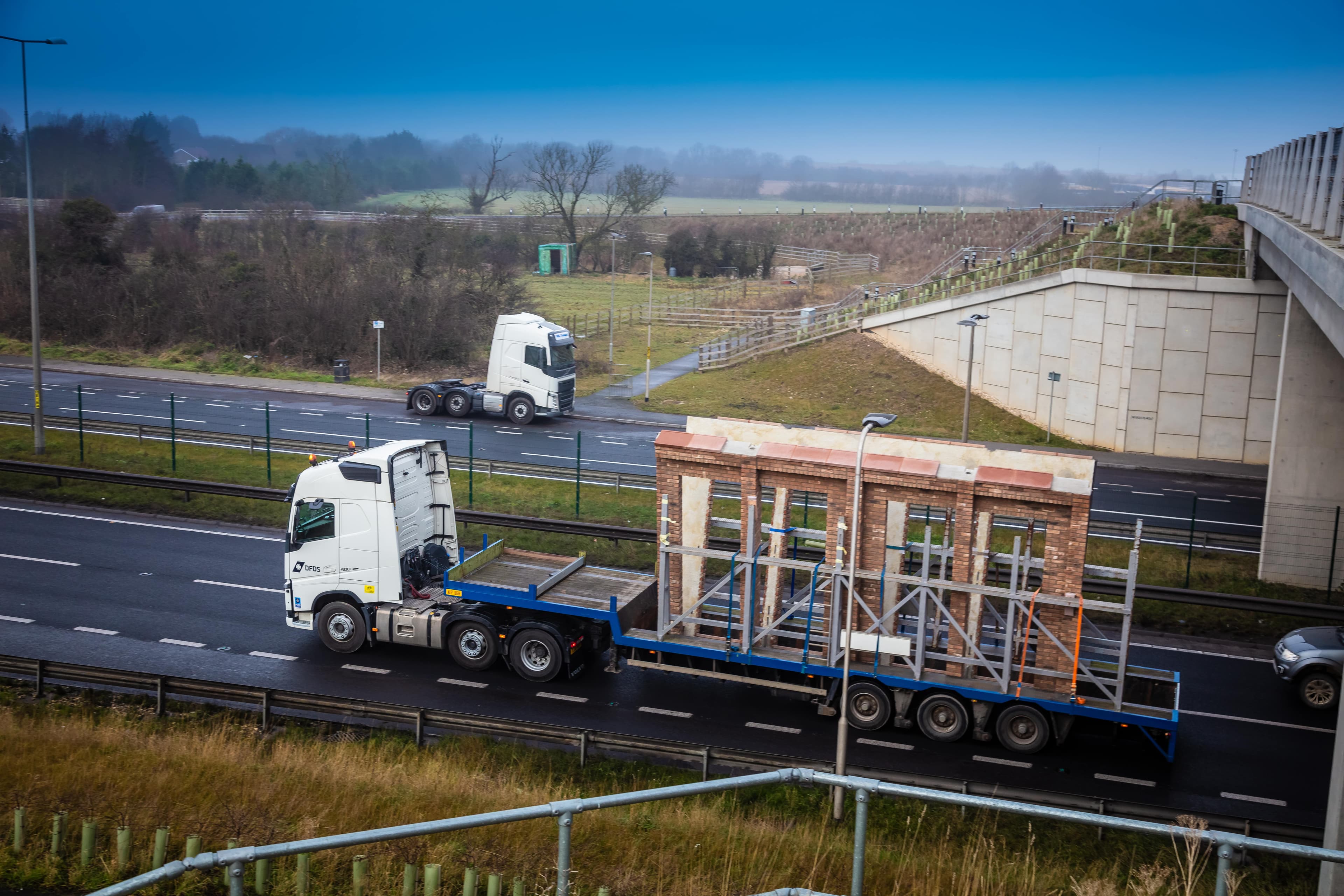 DFDS logistics truck transporting a façade made of light brown bricks, circulating on a national road