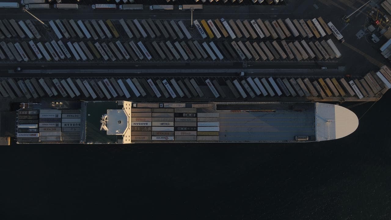 An aerial shot of a horizonal ship at dock next to trailers